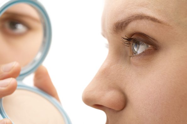 Woman after rhinoplasty looking in a compact mirror