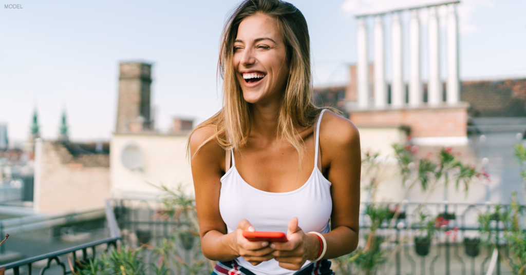 Young woman in white tank top laughing at something on her phone