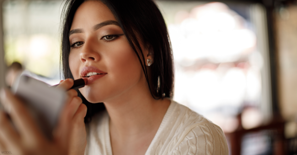 Woman applies lipstick to her full lips.