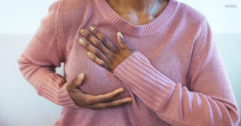 Woman (model) holding her breast while wearing a sweater.