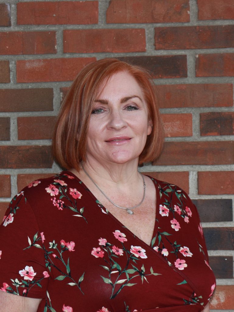 Christine DeFalco in red top with flowers in front of a brick wall