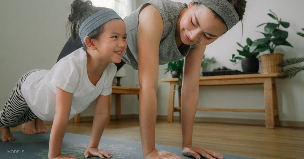 Mother and daughter (models) doing yoga together indoors.